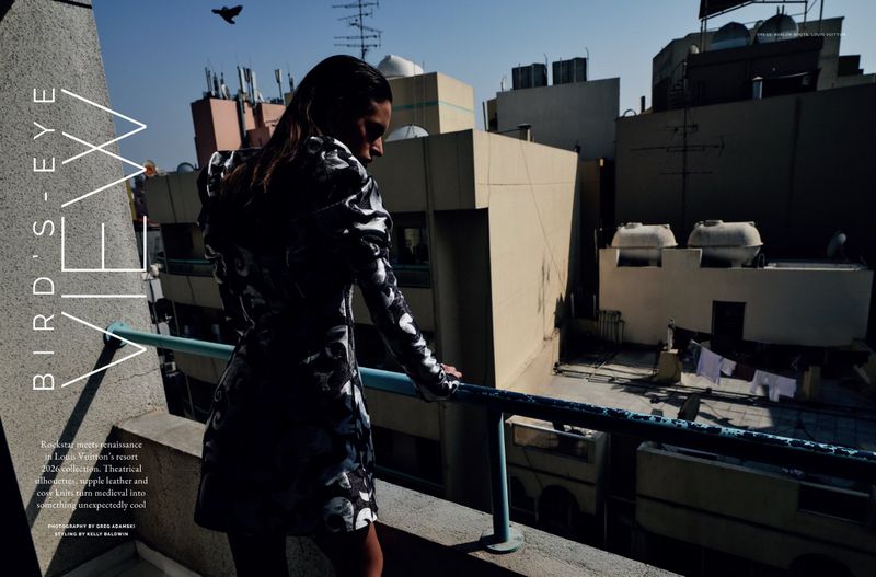 Woman in a black and white dress poses on a rooftop with buildings in the background under a clear sky in an editorial fashion shot.