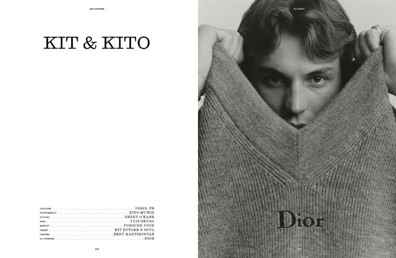Black and white portrait of a young adult man partially obscured by a gray Dior sweater he is holding up near his face.