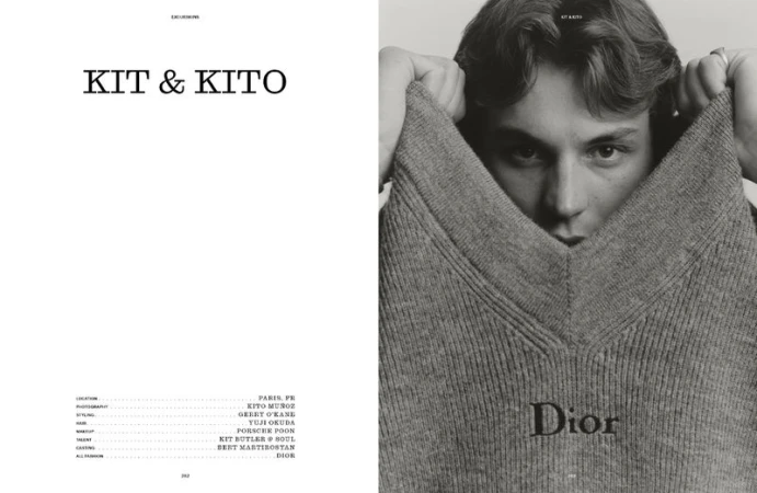 Black and white portrait of a young adult man partially obscured by a gray Dior sweater he is holding up near his face.
