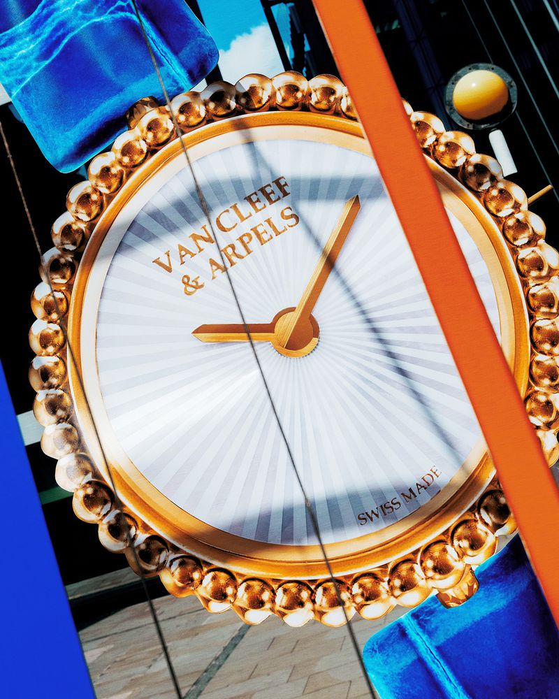 Close-up of Van Cleef & Arpels wristwatch featuring a white face with gold hands and beaded gold bezel, showcasing luxury timepiece.