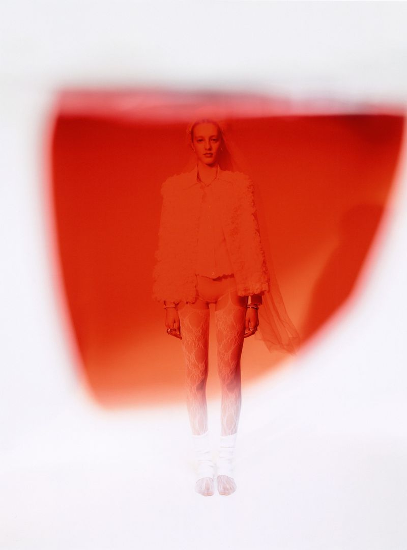 Woman stands in a fashion shot with an orange overlay, wearing a fuzzy jacket, leggings, and ankle boots in a bright studio.