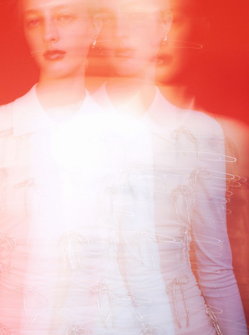 Model Ebba Bostrom wearing a white collared dress against a vibrant red background in a motion-blurred editorial portrait.