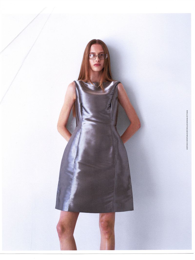 Woman with long red hair poses in a silver dress against a white backdrop. Fashion shoot with clean lines and a minimalist aesthetic.