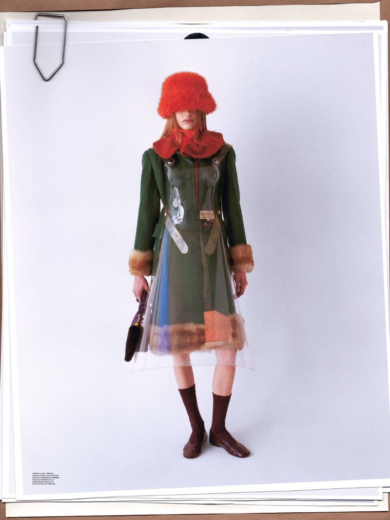 A fashion shot shows a model in a green jacket and clear dress, posing against a white backdrop with warm, natural lighting and a unique style.