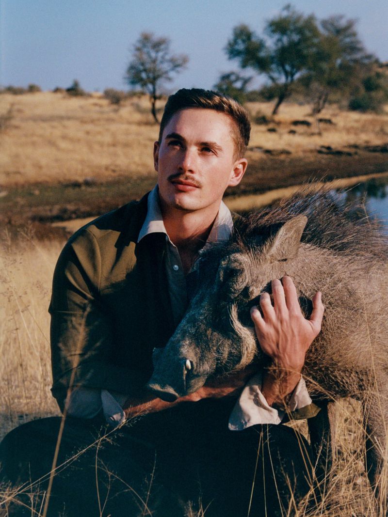 Man embraces a warthog in a sunny savanna, tall golden grasses, muted colors, contemplative mood, travel destination, wildlife photography.