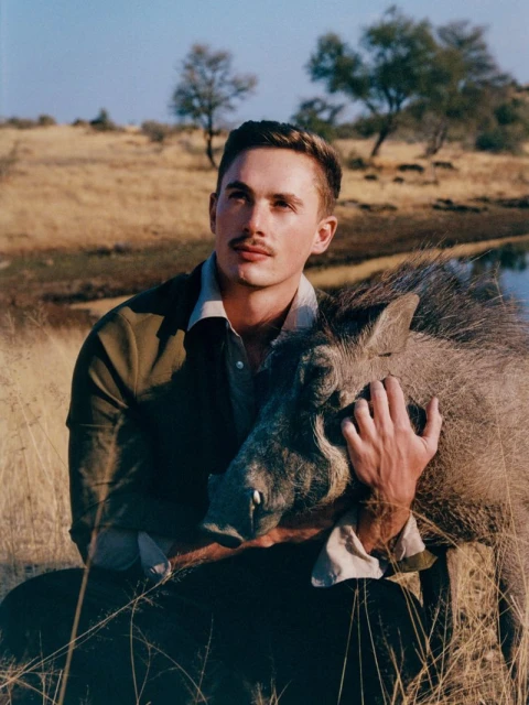 Man embraces a warthog in a sunny savanna, tall golden grasses, muted colors, contemplative mood, travel destination, wildlife photography.