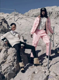Two female models posing on a rocky mountain slope wearing winter apparel including a pink puffer jacket and white knit sweater.