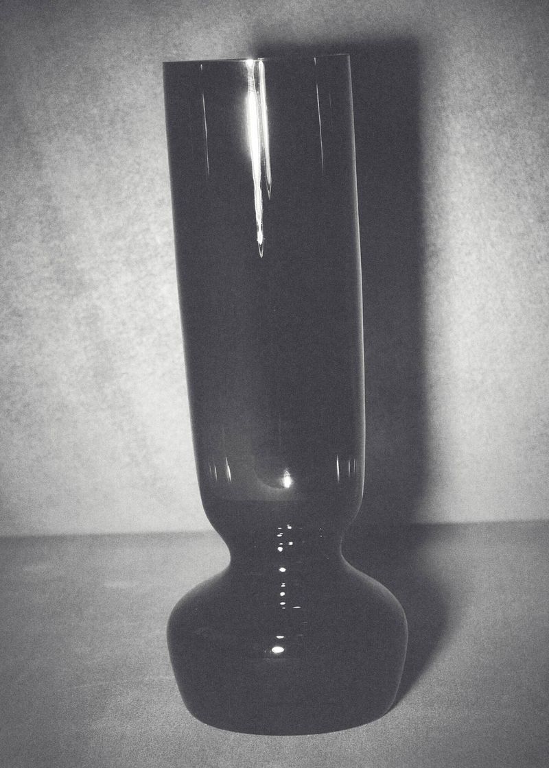Elegant tall black glass vase with glossy sheen, set against a muted background, showcasing minimalist design and subtle reflections.