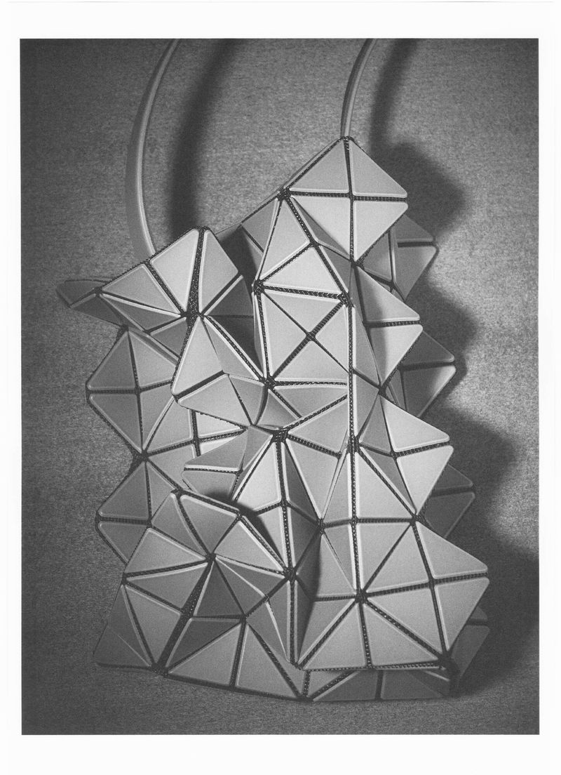 Black and white photograph of a geometric faceted handbag folded into an angular sculptural shape casting a dark shadow.