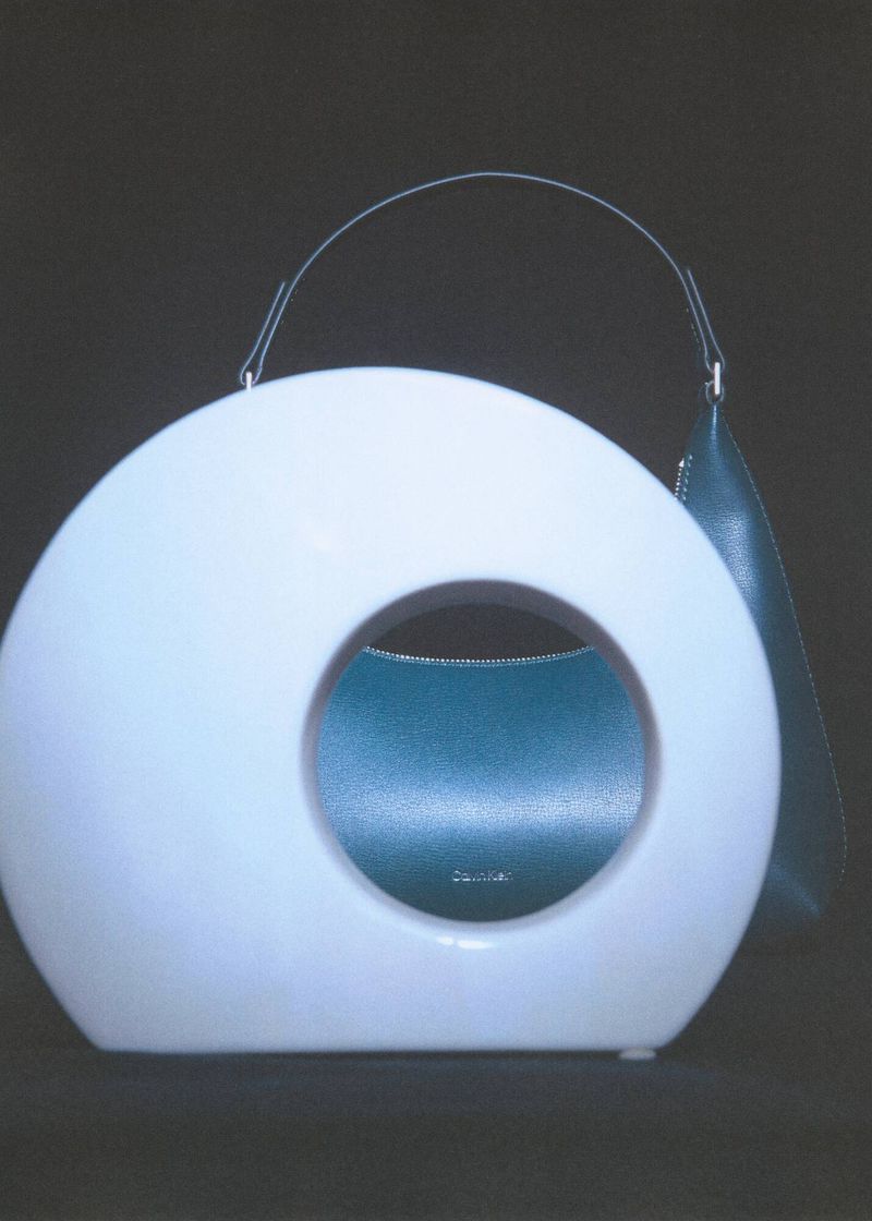 Fashion handbag featuring an unusual round, hollow design with a white exterior and teal interior against a dark background.