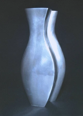 Sculptural brushed silver metallic vase with curved organic lines photographed against a dark black background.
