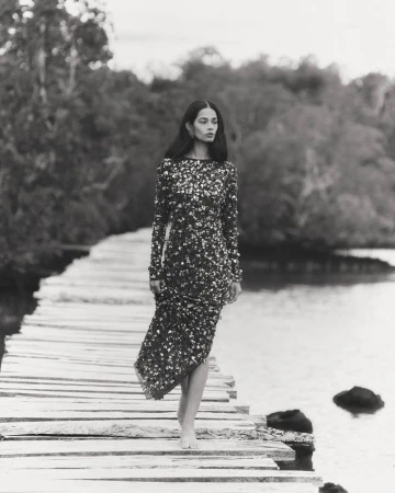 A striking black and white fashion shot featuring a lone woman in a sequined dress walking barefoot on a rustic wooden boardwalk.