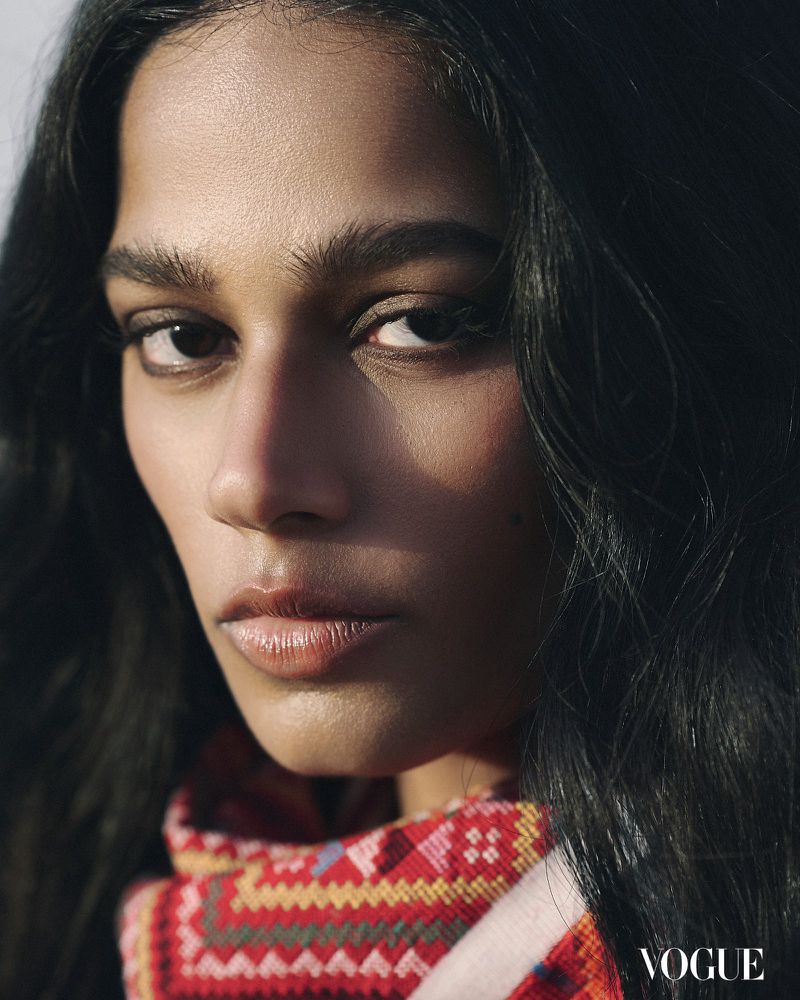 Close-up portrait of a dark-skinned woman with long dark hair, wearing a patterned scarf, and looking directly at the camera in a fashion editorial.