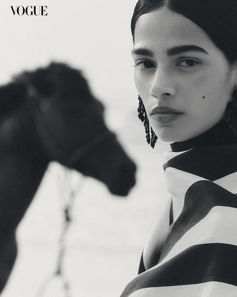 Black-and-white portrait of a woman with statement earrings and a black-and-white striped garment, and the partial view of a horse.