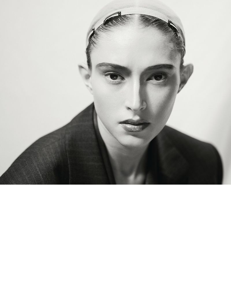Close-up portrait of a woman in a blazer with a neutral expression, wearing a headband, in a studio with soft, diffused lighting.