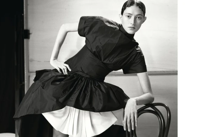 Monochrome fashion portrait of an adult female model posing in a stylish black and white dress while leaning on a black chair.