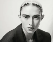 Black and white portrait of model Julia Rambukkana wearing a dark pinstripe blazer and hair clips against a pale background.