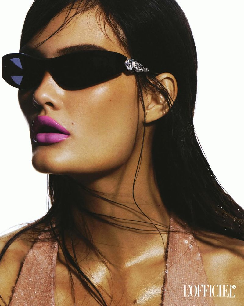 Close-up portrait of a woman with wet dark hair wearing black sunglasses and bright pink lipstick in a fashion style photograph.