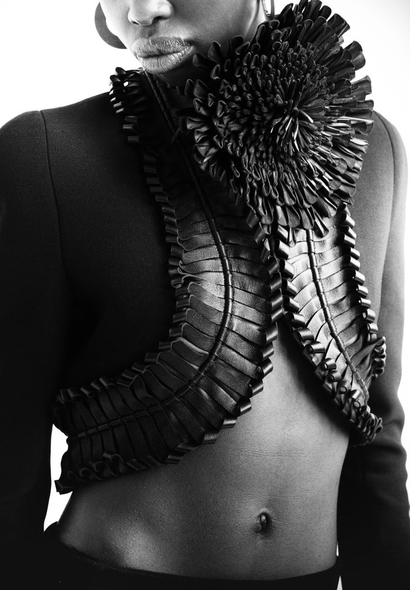 Elegant black and white fashion shot of a slim African American woman wearing a tailored jacket with textured, floral-style details.
