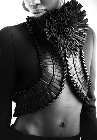 Elegant black and white fashion shot of a slim African American woman wearing a tailored jacket with textured, floral-style details.
