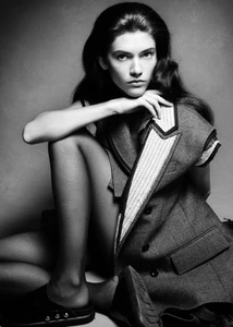 Model seated wearing a structured grey blazer with contrast lapels against a plain studio background.