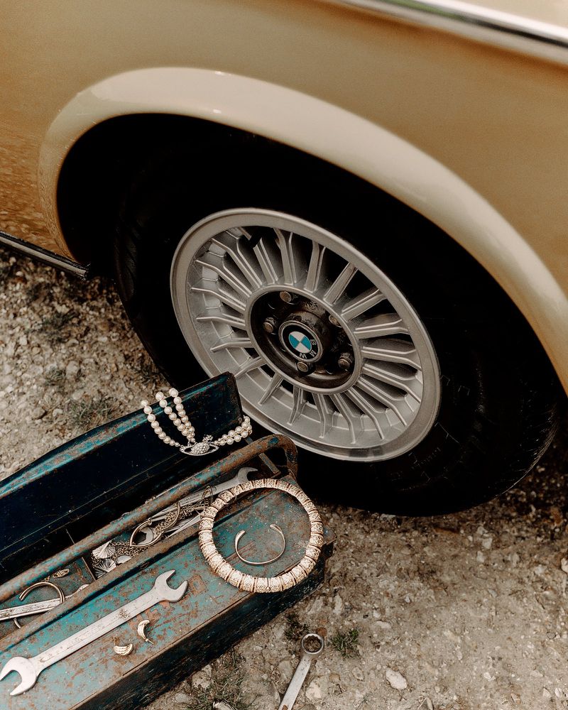 Vintage BMW wheel is positioned next to an open blue toolbox filled with wrenches and jewelry, creating a vintage aesthetic.