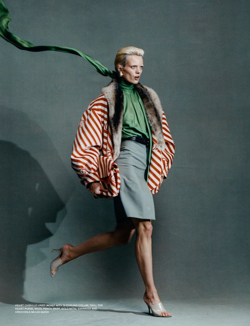 Fashion editorial image of a woman in a striped jacket and grey skirt, captured in a dynamic pose against a neutral backdrop.