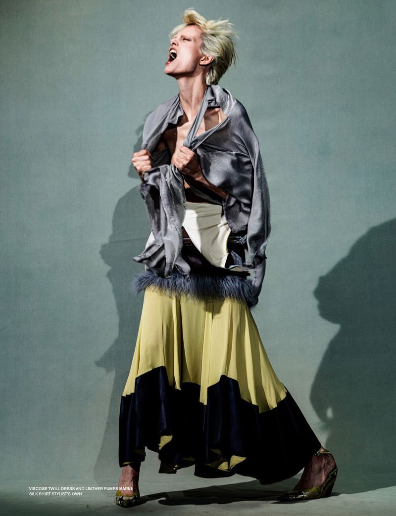 Editorial fashion shot of an adult female model in a gray silk top and yellow and black skirt posing in a photo studio with dramatic lighting.