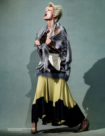 Editorial fashion shot of an adult female model in a gray silk top and yellow and black skirt posing in a photo studio with dramatic lighting.
