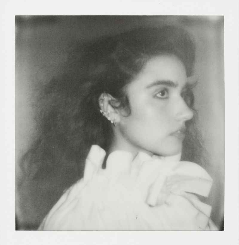 Black and white portrait of an adult woman in a white ruffled top with dramatic wavy hair and ear jewelry, captured in a profile view.