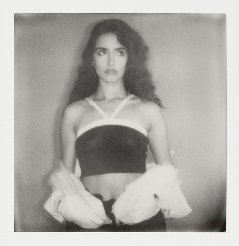 Monochrome portrait of a woman with long wavy hair, wearing a black top and jacket, looking up in an indoor setting.