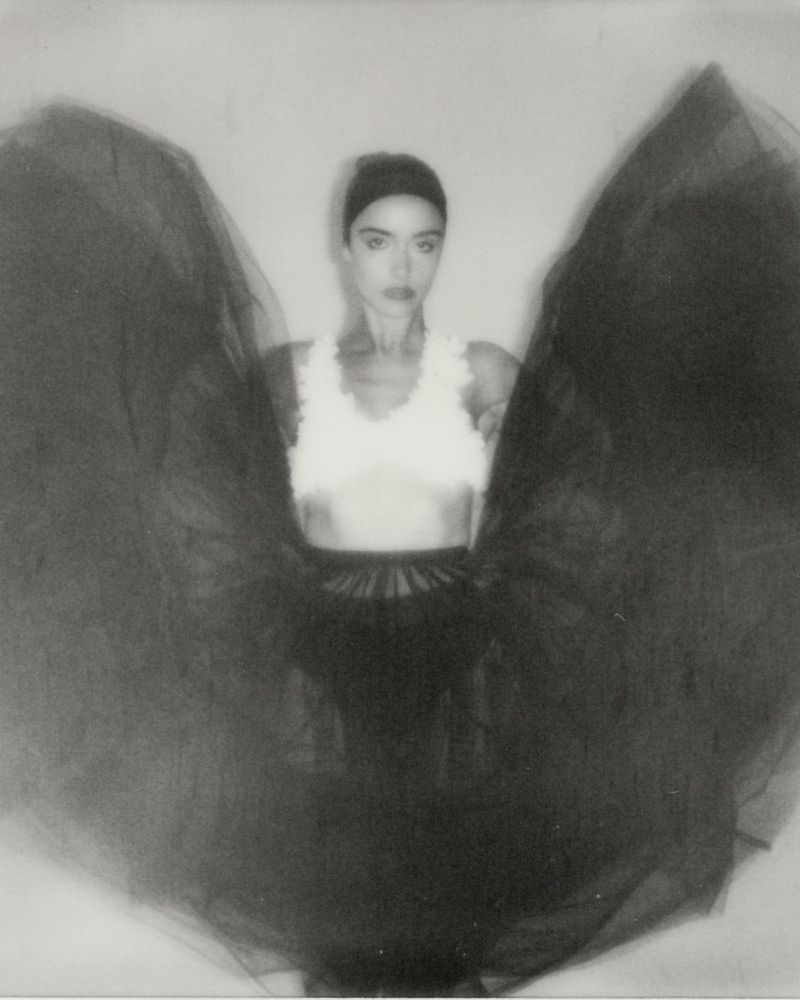 Portrait of woman in white top and black tulle skirt with intentional motion blur in a neutral indoor studio setting.