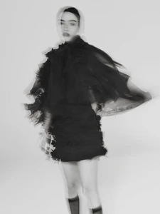 Model in a black ruffled sheer cape and skirt photographed with a multiple exposure blur effect against a light background