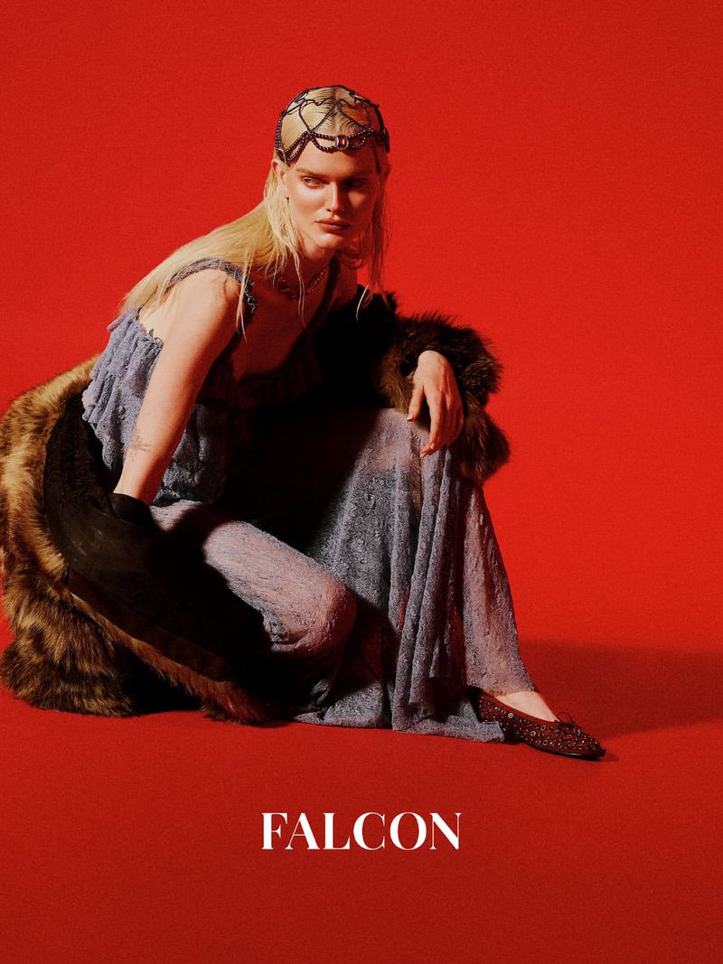 Fashion photo of a person with long blonde hair wearing a dress, fur stole, and beaded headpiece against a red background, studio shot.
