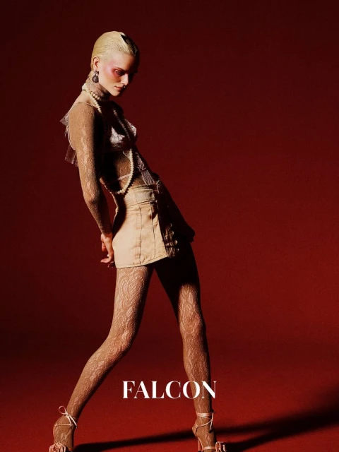 Fashionable woman in a pose with lace tights, a beige skirt, and a pearl necklace against a red background.