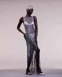 Model with platinum blonde hair wearing a silver netted fringe dress against a neutral studio background