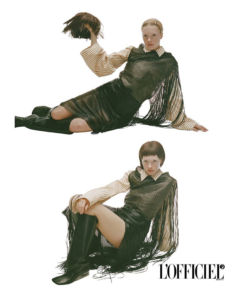 Fashion shot of a model in black fringe dress, striped shirt and tall boots lying on a white background and holding a hair piece.