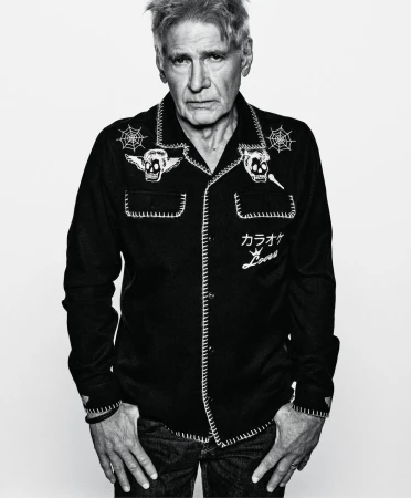 Monochrome portrait of Harrison Ford in a patterned black bowling shirt with skull and spiderweb graphics against a white background.