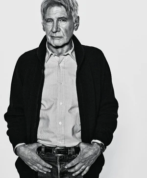Harrison Ford wearing a dark cardigan over a buttoned shirt and jeans against a plain light background