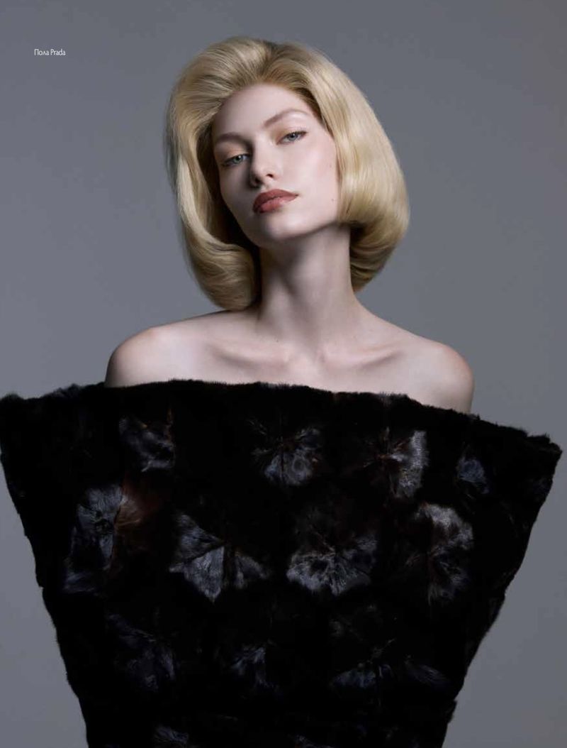 Blonde woman poses in a close-up fashion shot in front of a grey studio background, showcasing a black floral dress.