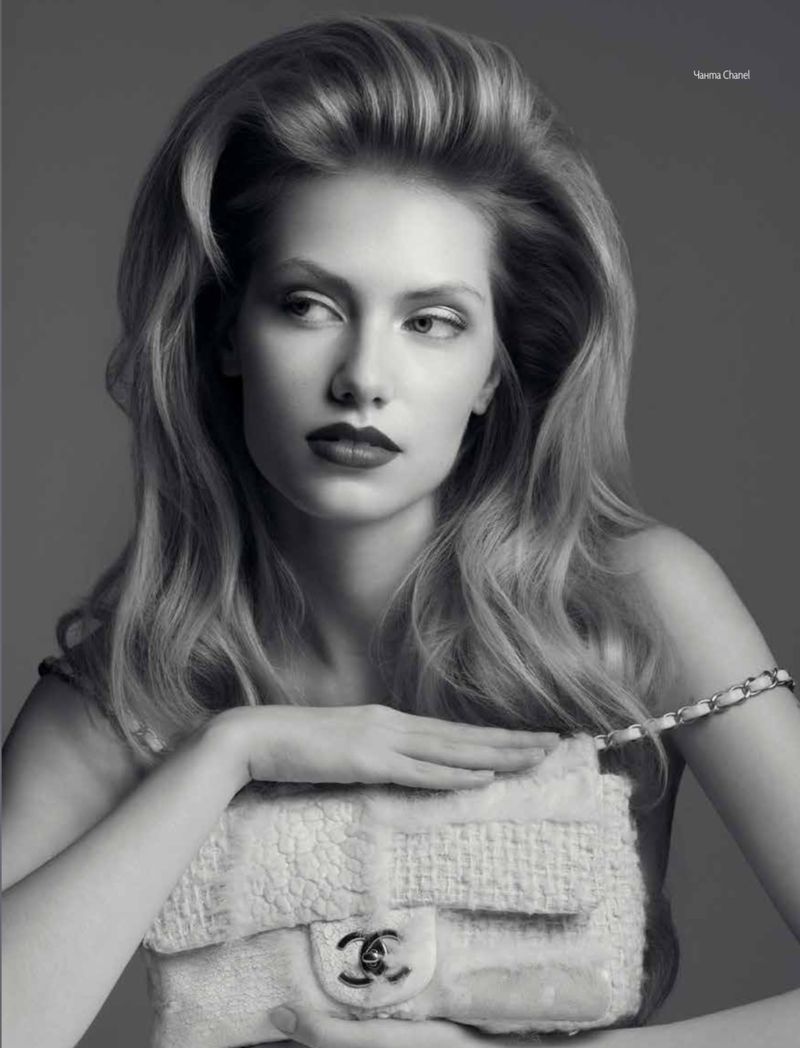 Black-and-white studio fashion portrait of a woman with long blonde hair holding a white Chanel handbag, looking off-camera.