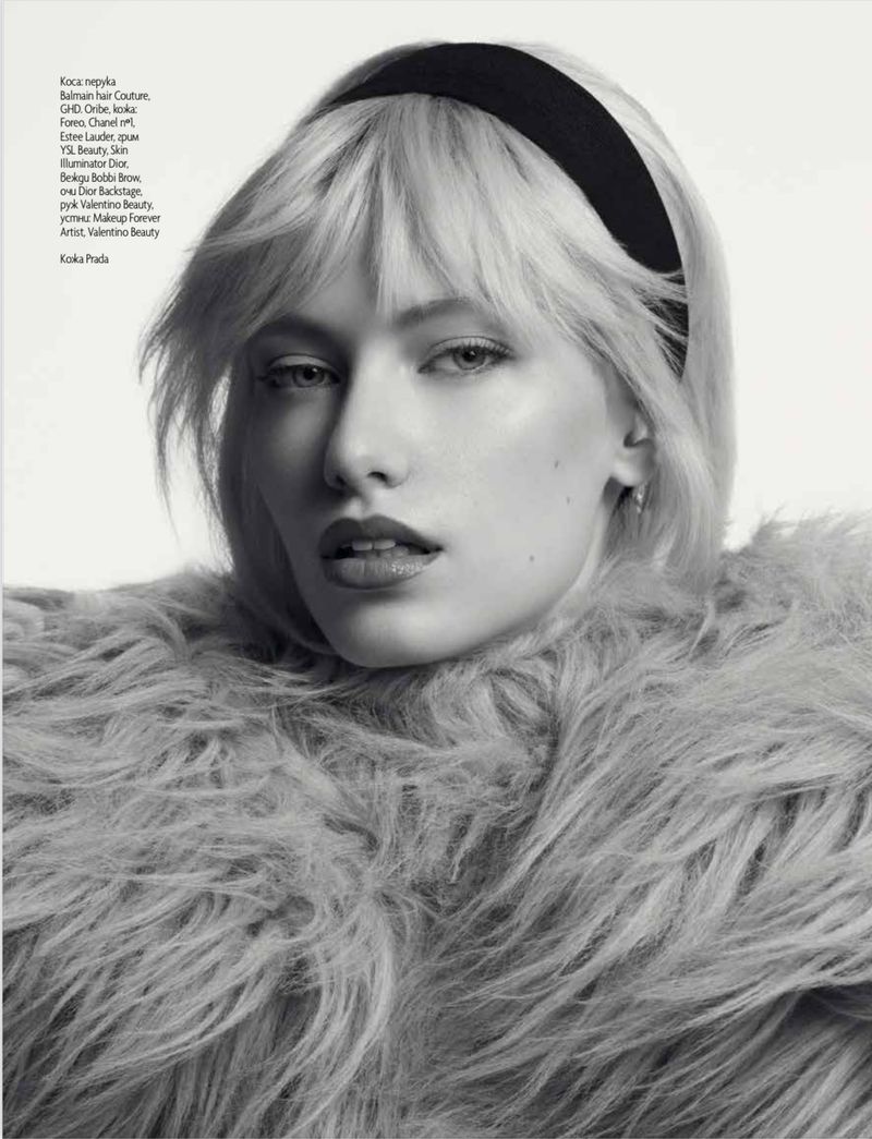 Portrait of a blonde woman wearing a black headband and a textured fur garment against a plain white background.