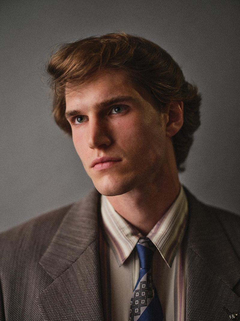 Portrait of Alberto Paolini wearing a grey suit jacket, striped shirt, and patterned blue tie against a grey studio backdrop.