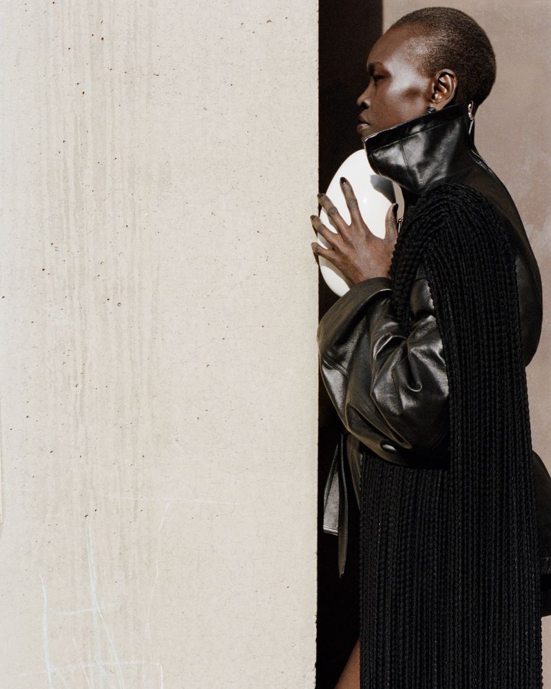 Fashion shot of black female adult holding white spherical prop, wearing black leather-look top and fringed shawl in studio.