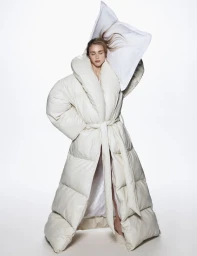 Model Hedvig Palm wearing a voluminous cream puffer coat holding a white pillow against a white background for Vogue Scandinavia