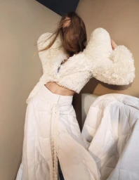 Model Hedvig Palm wearing a cropped white textured jacket and wide quilted trousers with her hair swept over her face.