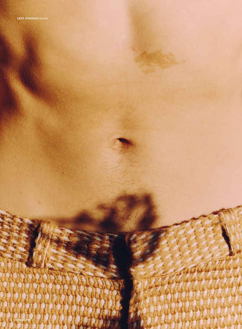 Close-up studio shot of a person's torso featuring fair skin, a navel, and the waistband of woven-texture tan pants.