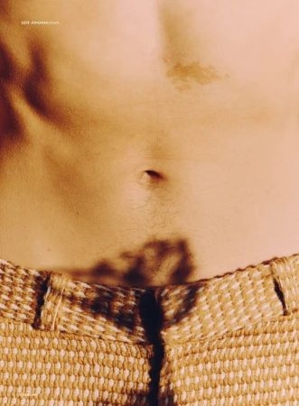 Close-up studio shot of a person's torso featuring fair skin, a navel, and the waistband of woven-texture tan pants.