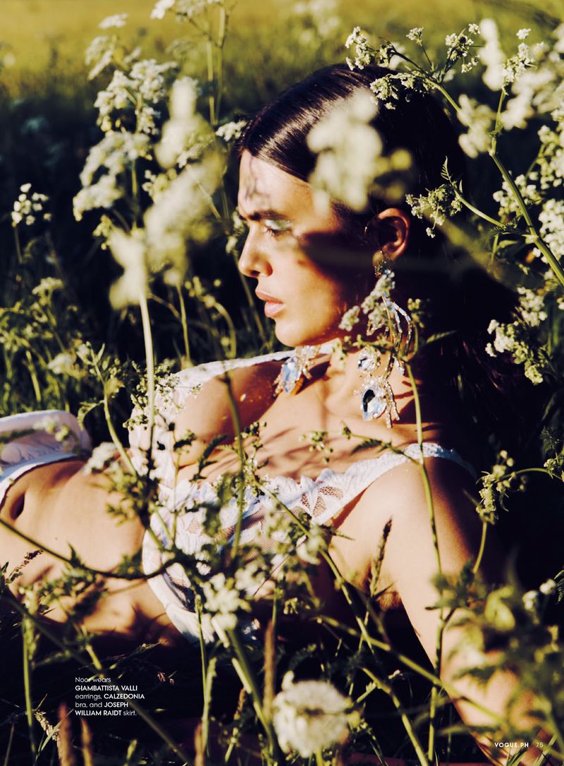 Model wearing white lace top and crystal earrings lying amidst tall white wildflowers