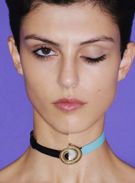 Close-up portrait of a young woman with half of her face and one eye visible. She wears a split color necklace with a gold clasp.